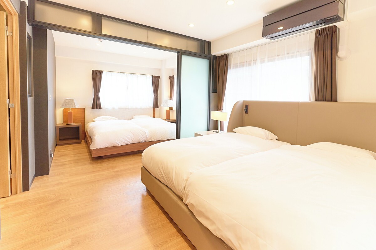 Ein Hotelzimmer mit einem großen Bett, einem zusätzlichen Bett, einem Schreibtisch und einem Fenster mit Vorhängen.
