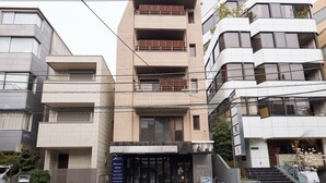 Un edificio de varios pisos con una planta baja comercial, que cuenta con un escaparate con señalización y una escalera que conduce a la entrada.
