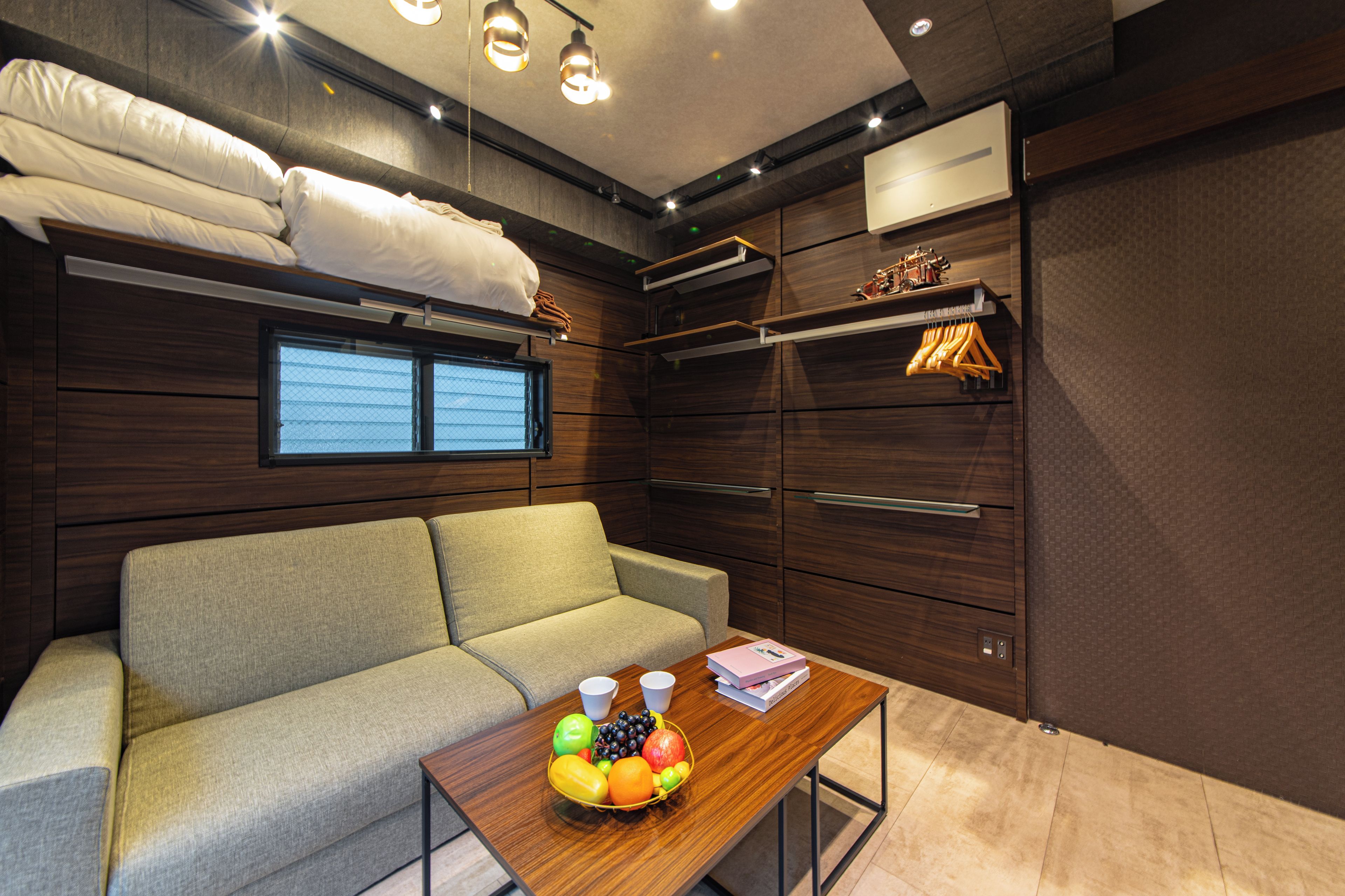 A compact living space with a sofa, a small table with fruit, a window, and built-in storage.
