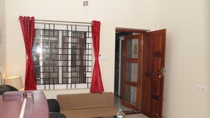 A living room with a sofa, a coffee table with a bottle, a window with metal bars, and a wooden door. - Jayam Residency (Tiruvannamalai)