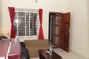 Una sala de estar con un sofá, una mesa de centro con una botella, una ventana con barrotes y una puerta de madera.