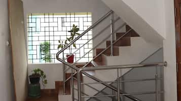 A staircase with metal railings leading to a landing, a window with a view of greenery, and a door on the left.