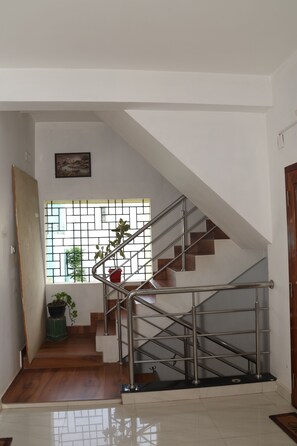 A staircase with metal railings leading to a landing, a window with a view of greenery, and a door on the left. - Jayam Residency (Tiruvannamalai)