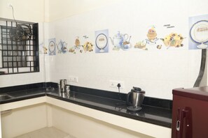 Una cocina con salpicadero de azulejos blancos, encimera negra, electrodomésticos de acero inoxidable y una ventana con reja de metal.