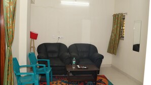 A living room with a sofa, a small table, a blue chair, and a patterned rug. - Jayam Residency (Tiruvannamalai)