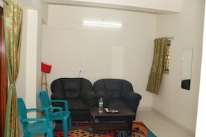 Una sala de estar con un sofá, una mesita, una silla azul y una alfombra estampada.