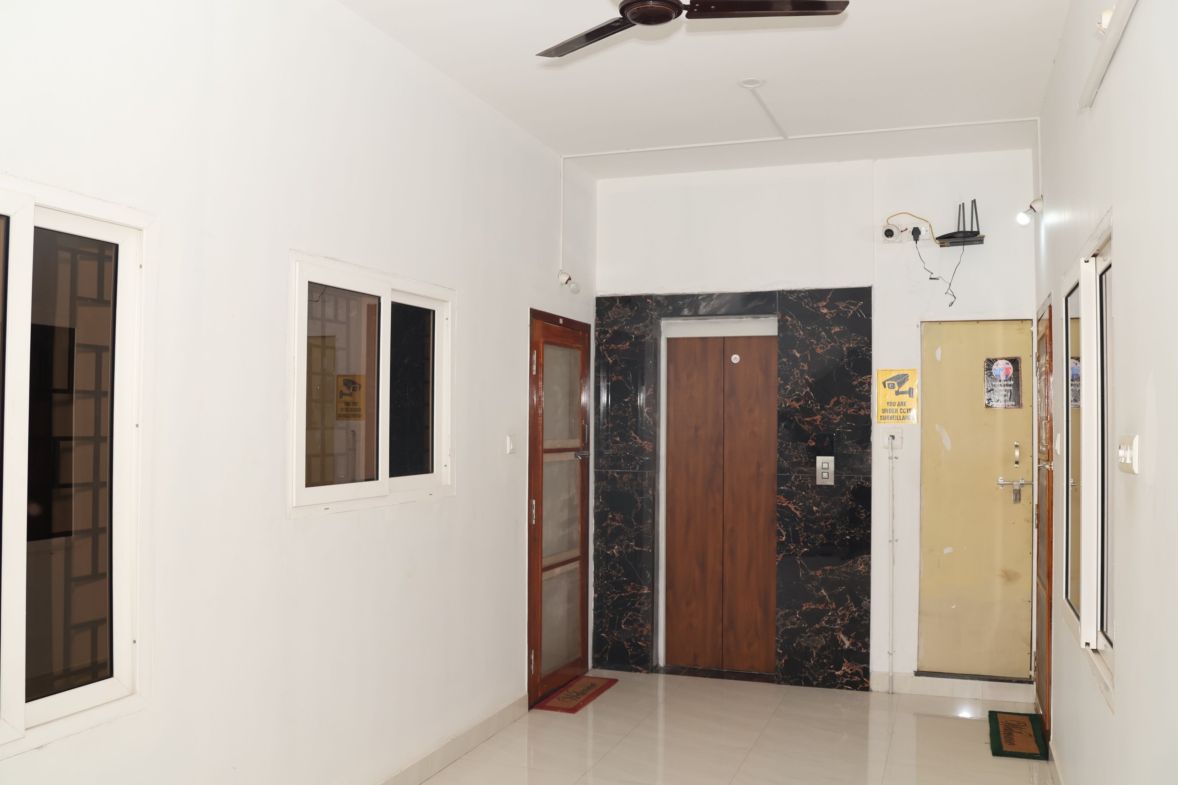 A hallway with a ceiling fan, a door with a marble surround, and a wall-mounted security camera.