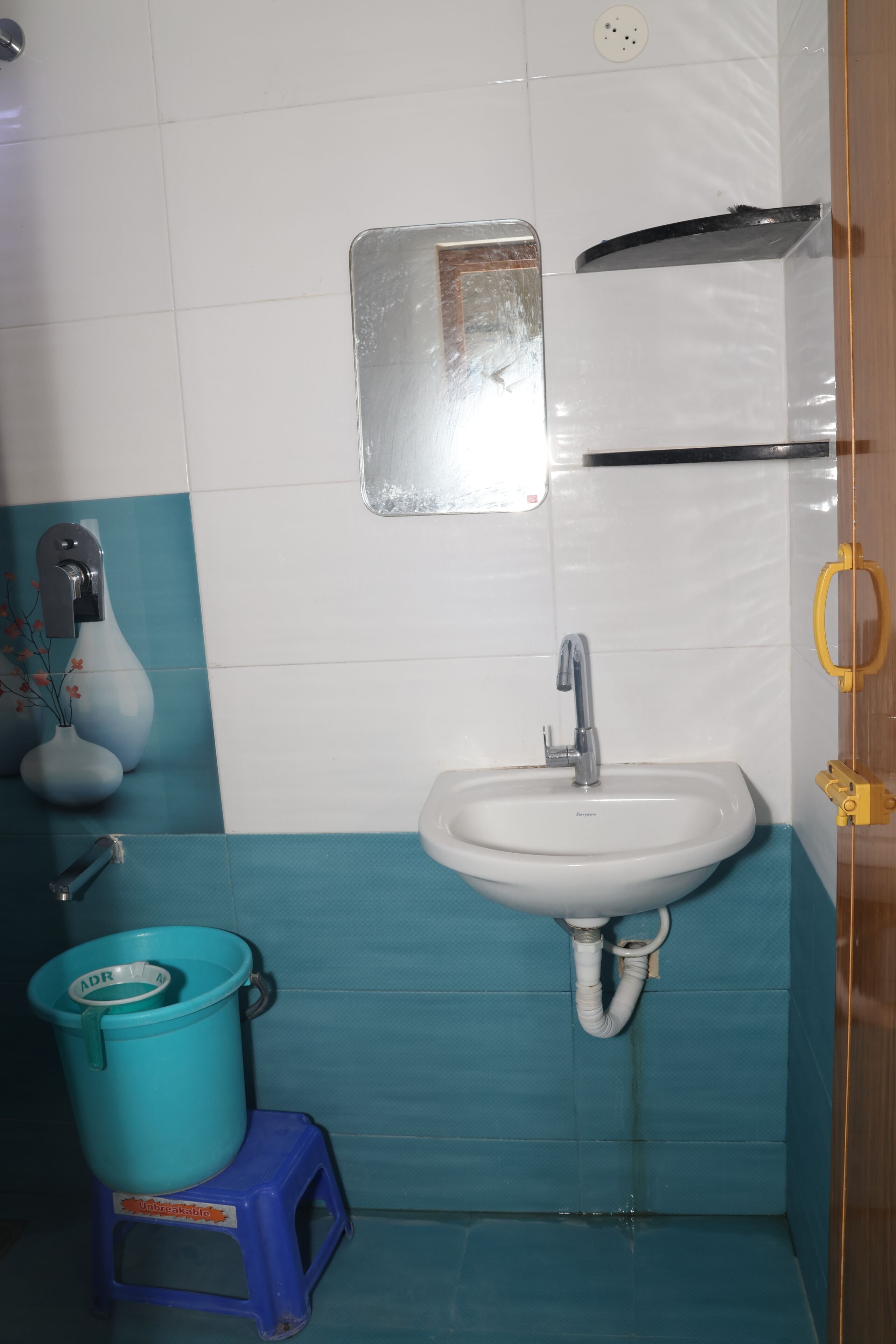 Een badkamer met een wastafel, spiegel en een blauwe prullenbak.