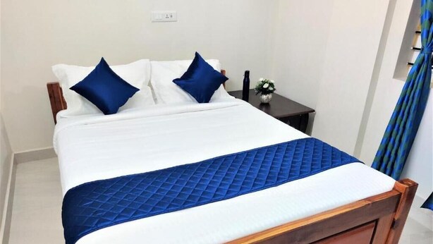 A bed with a wooden frame, white bedding, and blue accents. - Jayam Residency (Tiruvannamalai)