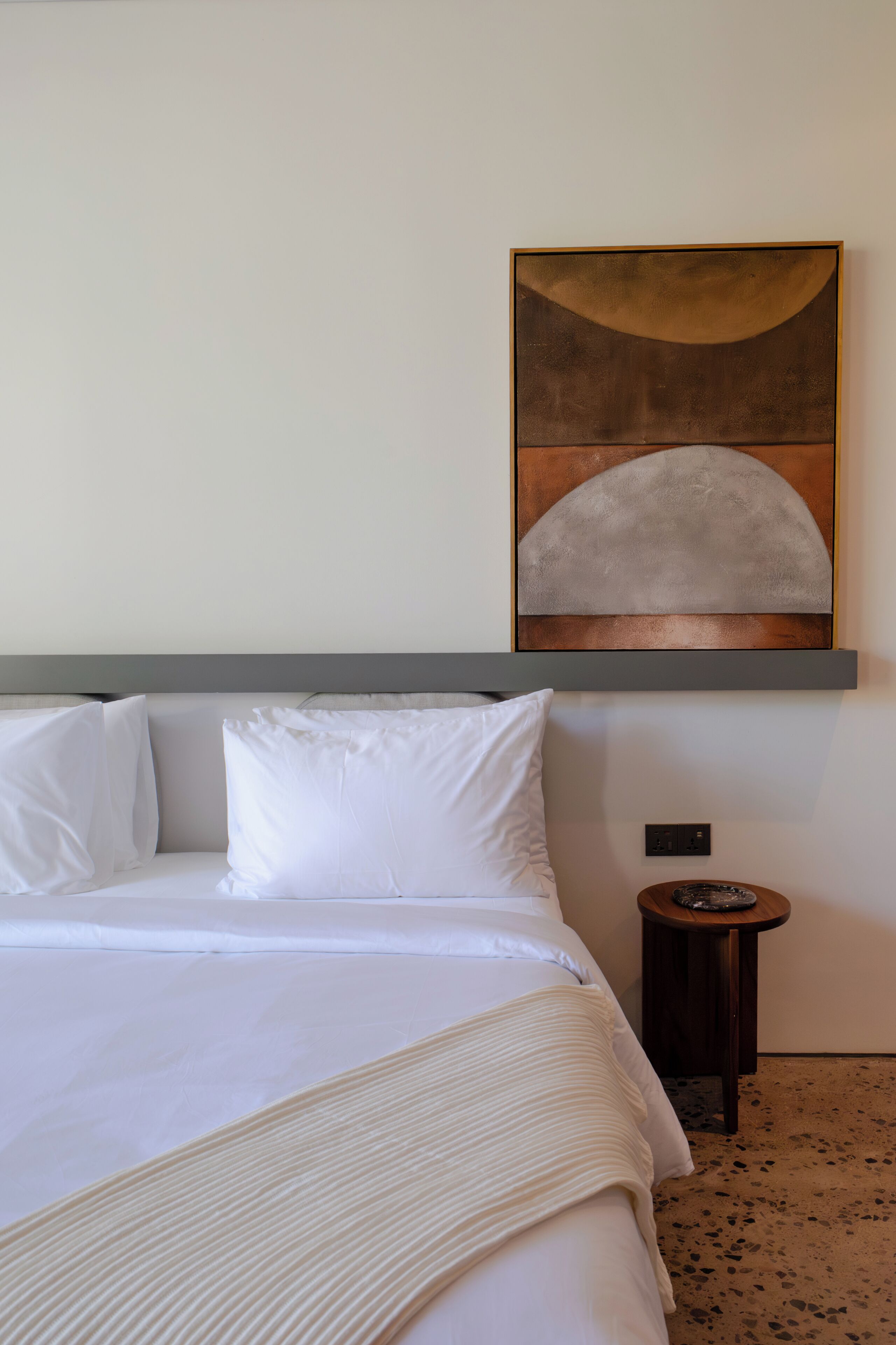 A neatly made bed with white linens, a headboard, and a small bedside table with a lamp.