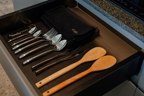 A drawer with a black interior containing a set of silverware, wooden spoons, and a black napkin holder. - Ecoverse Resort & Residence by OXO - Nyanyi Beach, Bali (Tabanan)