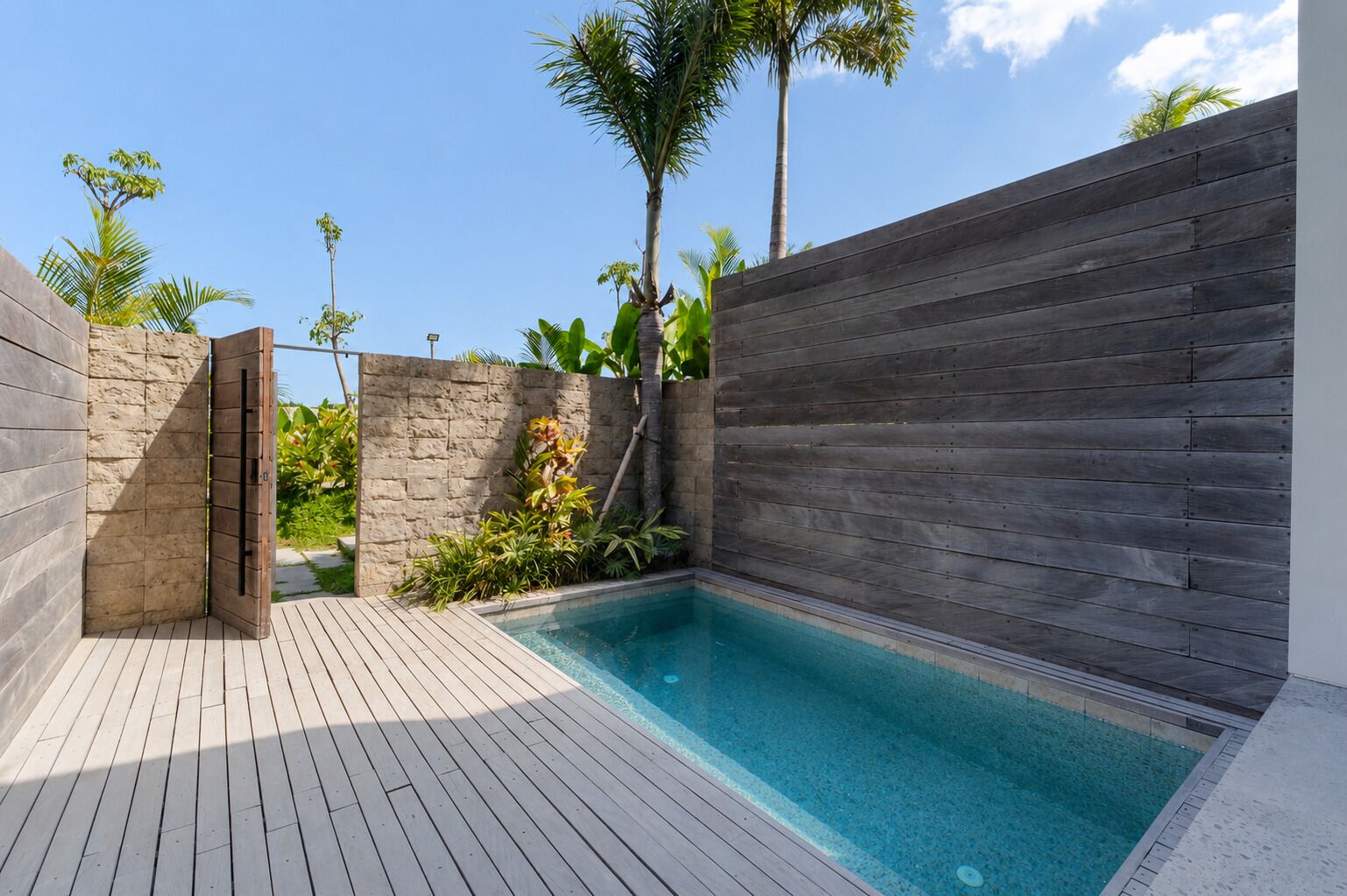 Une piscine dotée d’une terrasse en bois, entourée d’un mur de pierre et d’une clôture en bois.