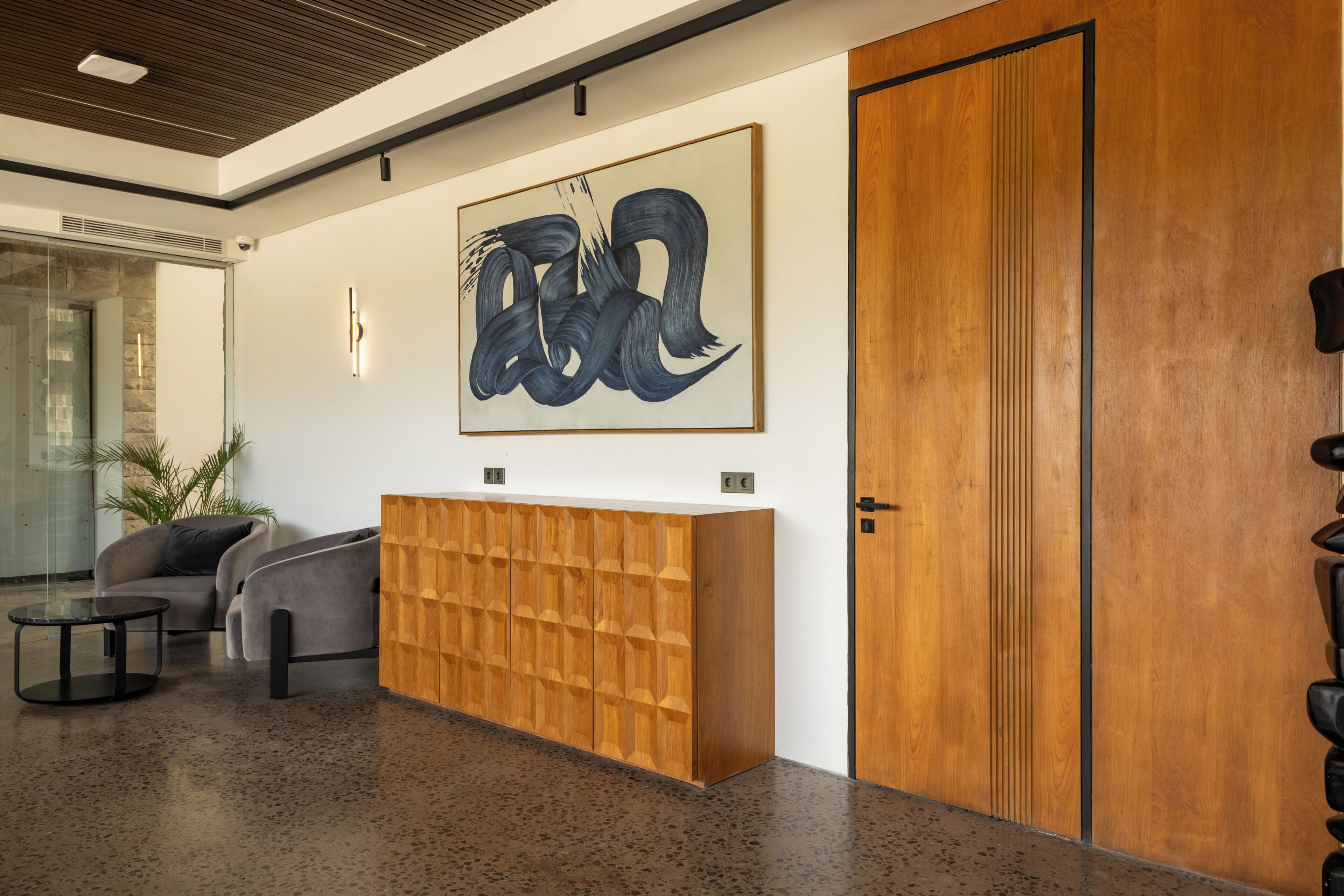 Un área de recepción con un mostrador de madera, un cuadro abstracto grande, un sofá gris y una puerta.