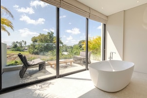 A modern bathroom with a freestanding bathtub, large windows, and a view of a garden.
