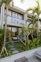 A modern building with large windows, a balcony, and a garden with palm trees and a wooden deck.