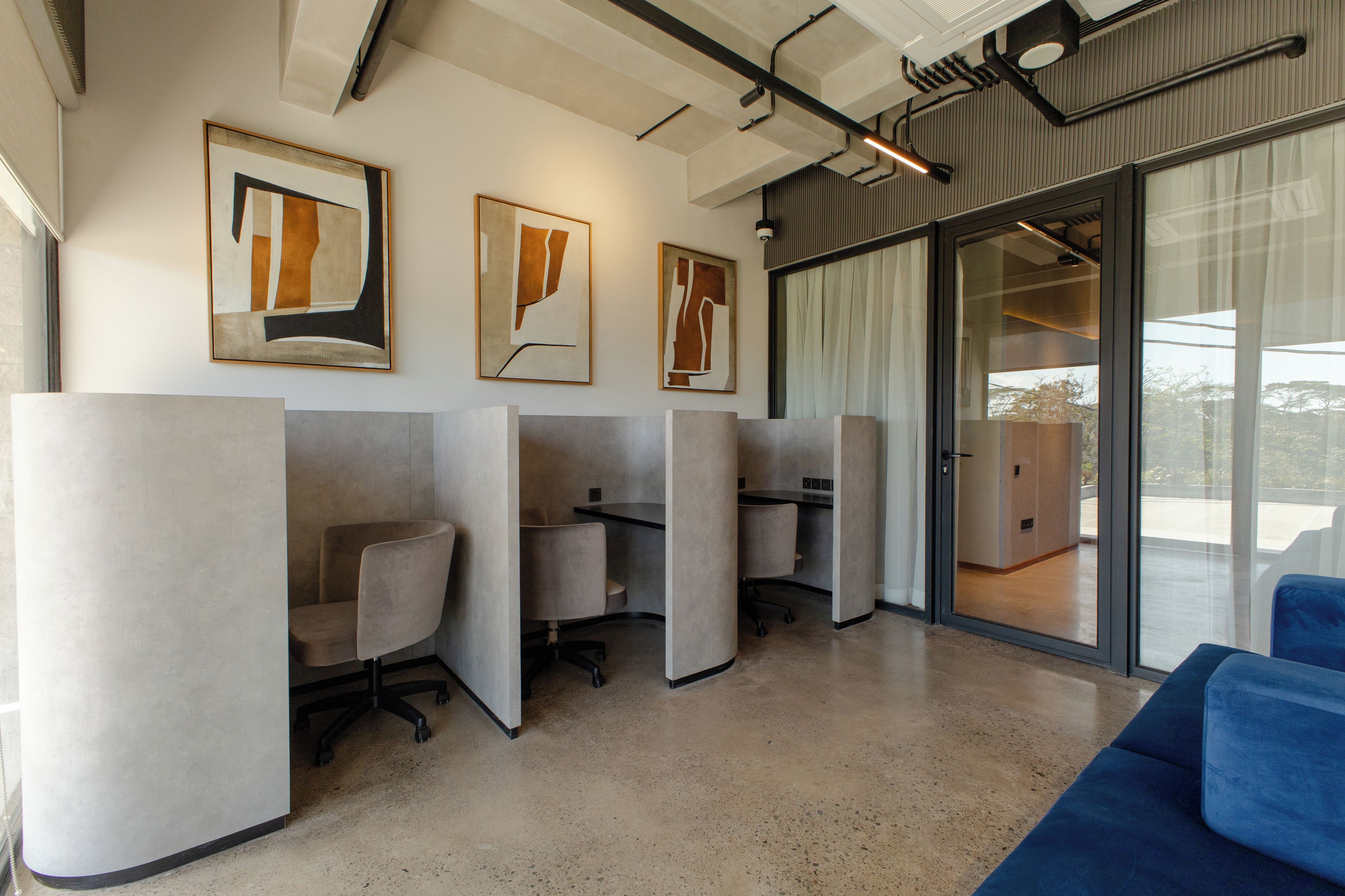 A modern office space with cubicles, a blue sofa, and abstract art on the walls.