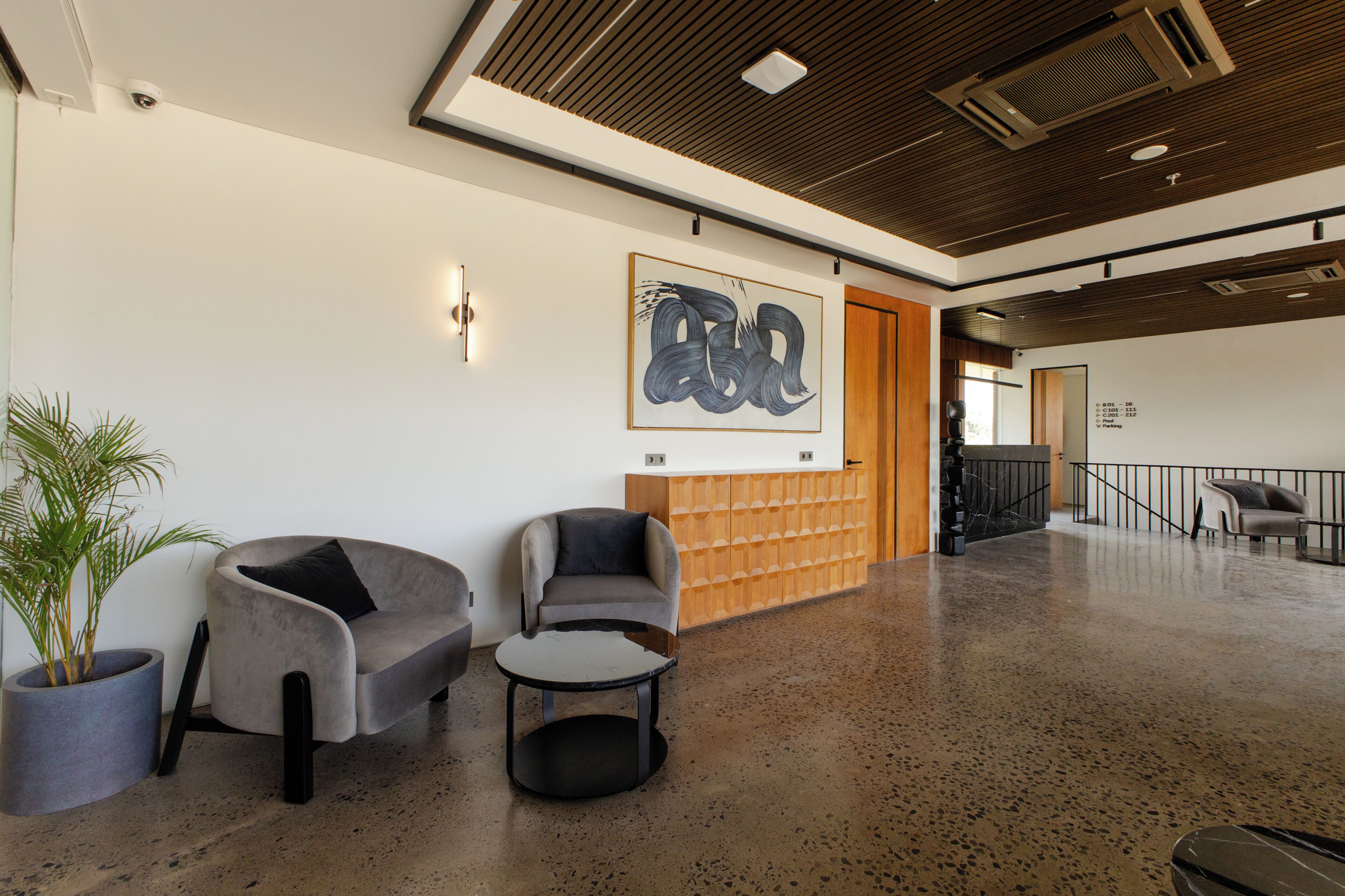 A lobby with two grey armchairs, a coffee table, a reception desk, and a wall-mounted artwork.