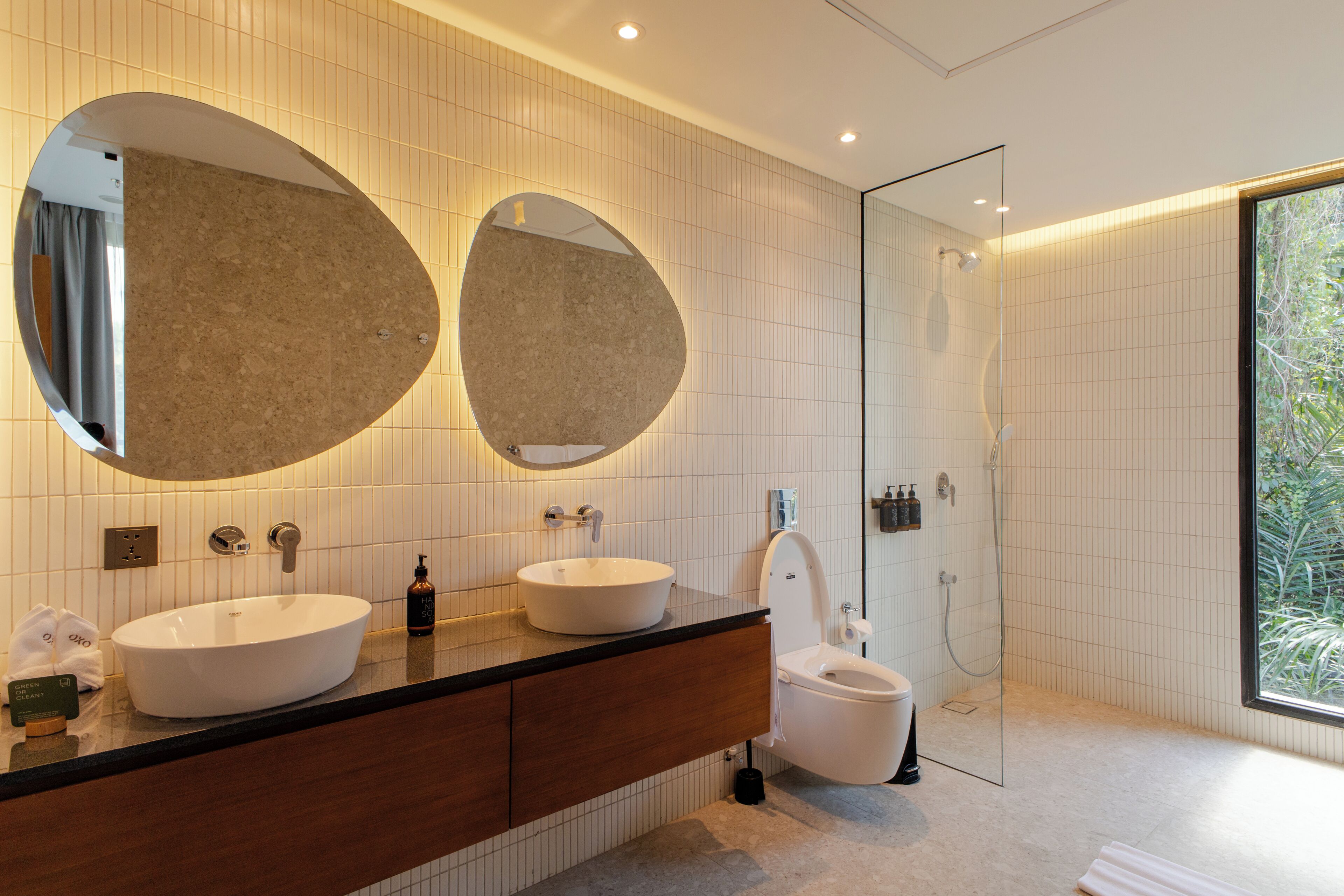 Un baño moderno con dos espejos ovalados grandes, un tocador doble, un inodoro y una zona de ducha.
