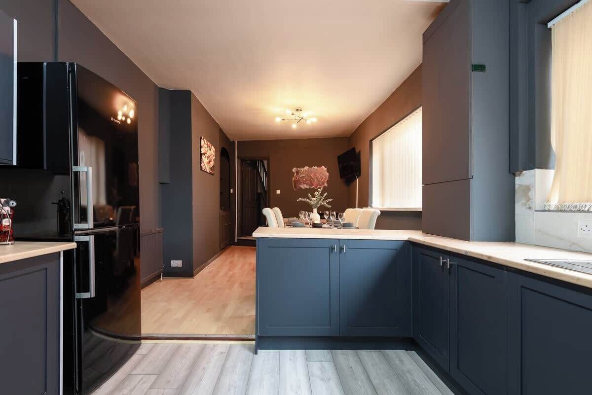 Une cuisine moderne avec des meubles de couleur sombre, un îlot central et un coin repas avec des chaises.