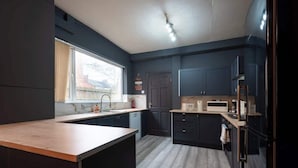 Cozinha moderna com armários escuros, bancada de madeira e janela que permite a entrada de luz natural.
