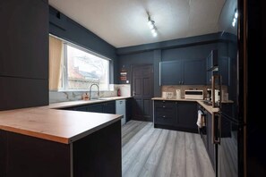 A modern kitchen with dark cabinetry, a wooden countertop, and a window providing natural light. - Largest Spacious 5 Bed Home w/ Garden & Games Parking near Hull Uni (Kingston upon Hull)