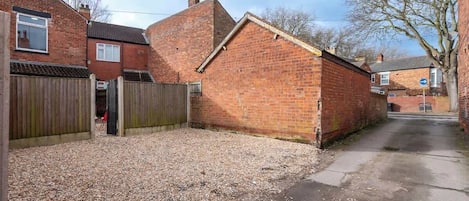 A residential area with a gravel driveway, a wooden fence, and a brick building.