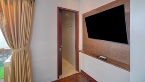 Ein Zimmer mit an der Wand befestigtem Fernseher, einer Tür zu einem anderen Raum und einem Vorhang am Fenster.