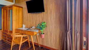 Ein Zimmer mit Holzboden, einem Fernseher, einem Schreibtisch, einem Stuhl und einer Topfpflanze.