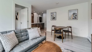A modern living room with a gray sofa, two wooden chairs, a coffee table, and two abstract paintings on the wall. - Luxury Apartment in Central Downtown Location (Vancouver)