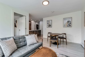 A modern living room with a gray sofa, two wooden chairs, a coffee table, and two abstract paintings on the wall.