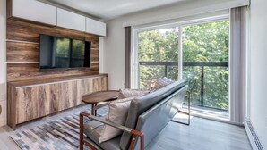 A modern living room with a built-in TV, a sofa, and a large window with a view of trees. - Luxury Apartment in Central Downtown Location (Vancouver)