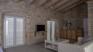 Un soggiorno con pareti in pietra, una TV a schermo piatto, un divano bianco e un tavolino da caffè in vetro.