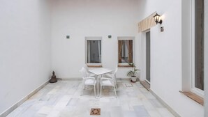 Un piccolo patio recintato con tavolo e sedie bianche, una pianta in vaso e un soffitto in legno.