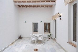 A small, enclosed patio area with a white table and chairs, a potted plant, and a wooden ceiling. - Guestready - Casa Palacio De La Cruz (El Puerto de Santa Maria)