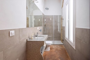 A bathroom with a granite countertop sink, a toilet, a glass shower enclosure, and a large mirror.