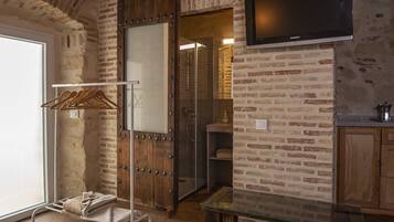 Una habitación con pared de ladrillo, puerta de madera, mesa de vidrio y televisor montado en la pared.