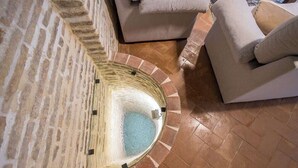 Una stanza con pareti in pietra, una fontana circolare, un divano beige e un pavimento decorato.