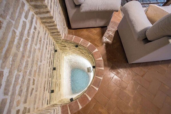 A stone-walled room with a circular water feature, a beige sofa, and a patterned floor. - Guestready - Casa Palacio De La Cruz (El Puerto de Santa Maria)