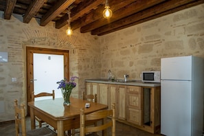 A rustic kitchen with a wooden table, a white refrigerator, and a stone wall. - Guestready - Casa Palacio De La Cruz (El Puerto de Santa Maria)