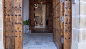 Una porta di legno con borchie di metallo, che dà su un interno a pareti in pietra e pavimento piastrellato.