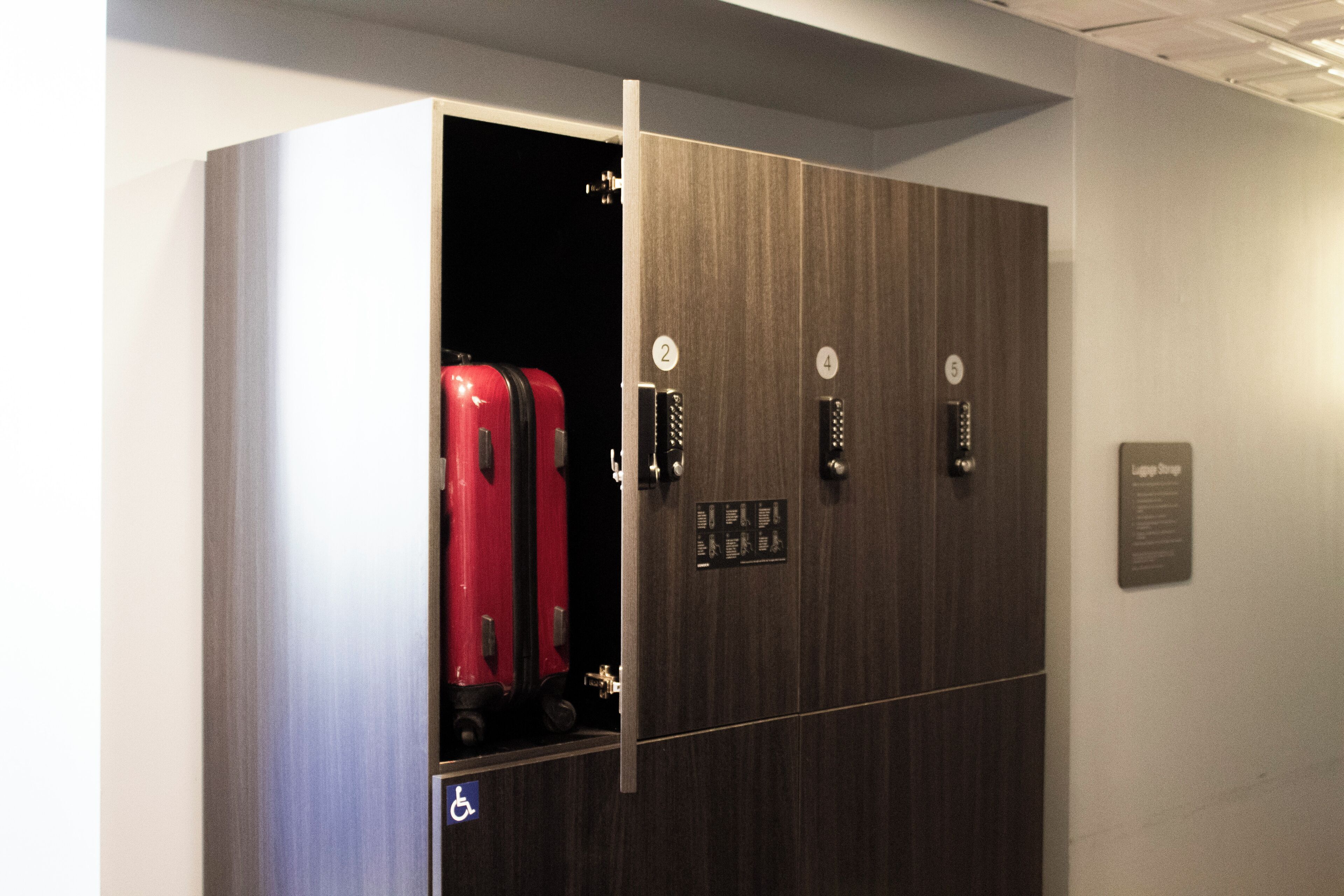 An elevator with numbered doors, a wheelchair accessibility sign, and a luggage compartment with a red suitcase.