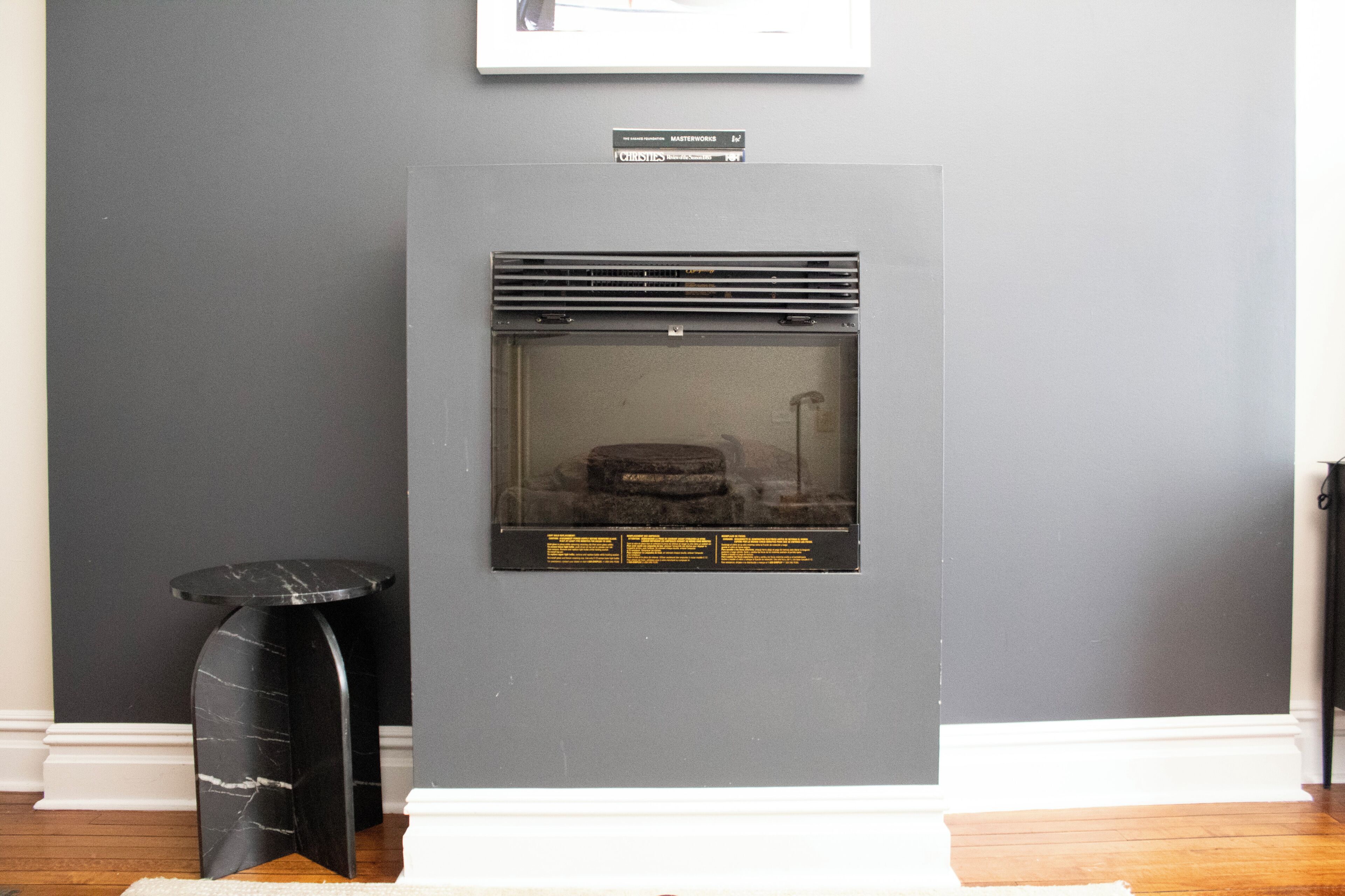 A fireplace with a glass front, a black marble side table, and a framed picture on the wall.