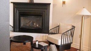 Una habitación con chimenea, una silla, una mesita y una lámpara de pie.
