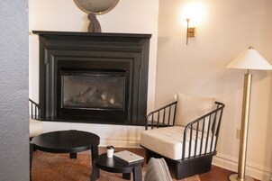 Una habitación con chimenea, una silla, una mesita y una lámpara de pie.