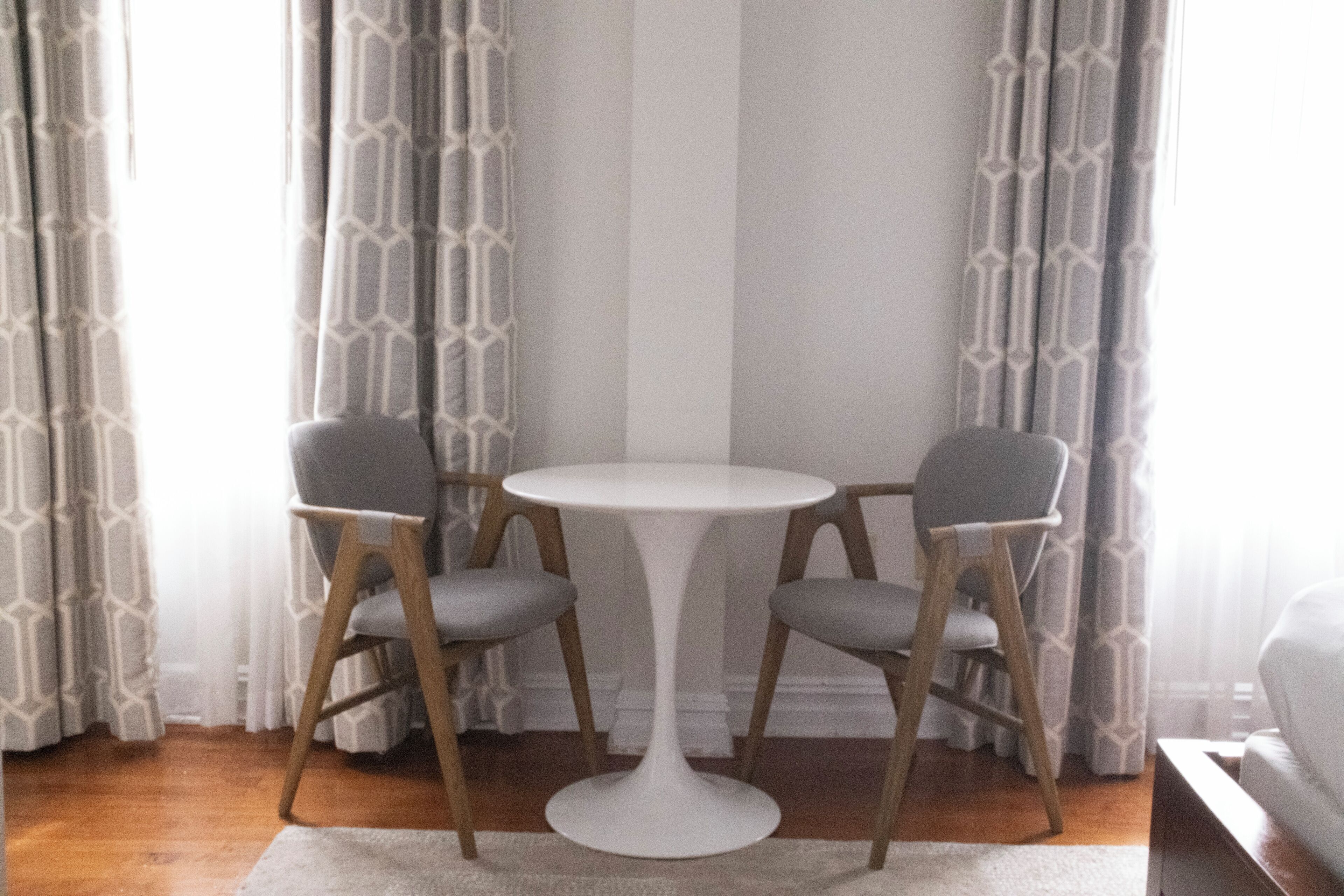 Une pièce avec une table ronde blanche, deux chaises grises et des rideaux à motifs.