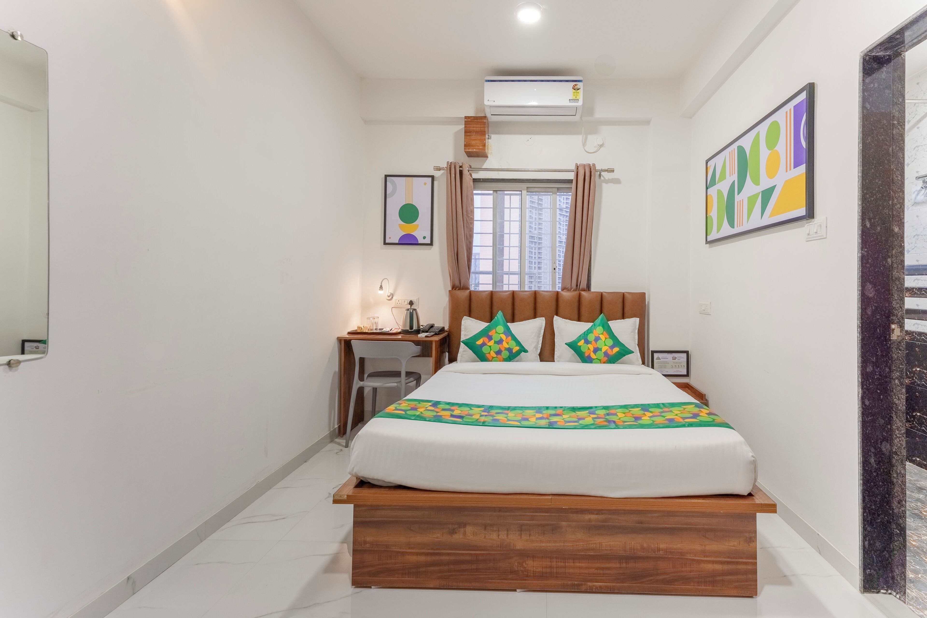 A bedroom with a wooden bed, a desk with a chair, a window with curtains, and a wall-mounted air conditioner.
