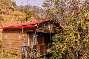 Una cabaña de madera con techo rojo, un balcón y montañas al fondo.
