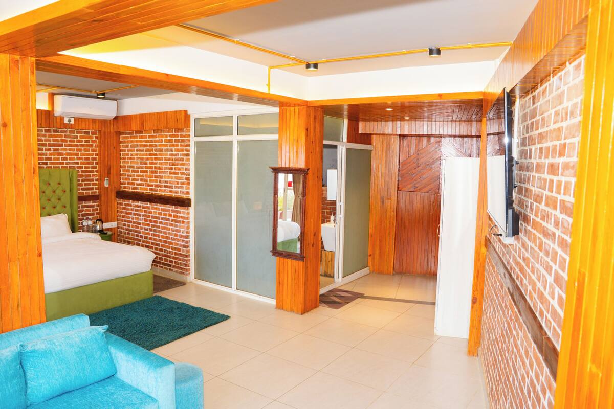 A hotel room with a brick wall, a bed, a green sofa, and a sliding glass door leading to a bathroom.
