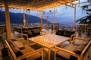 A rooftop terrace with wooden furniture, hanging plants, and a city view. - Lamatar Hills Resort  (Lamatar)