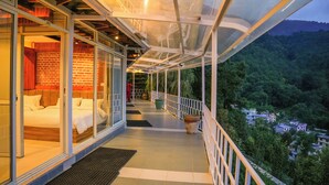 Un balcon doté d’une paroi vitrée, un lit et une vue sur une zone boisée.